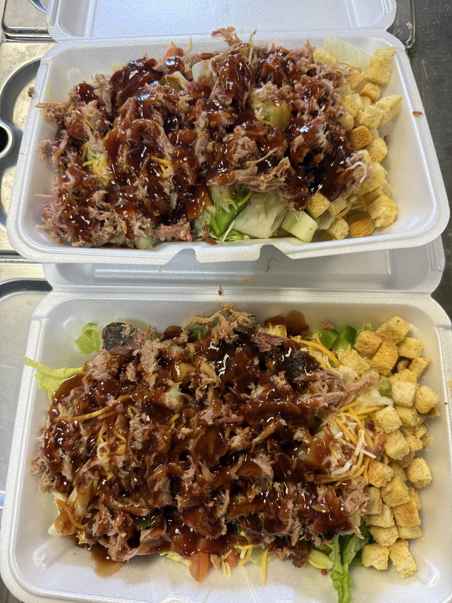 Two salads topped with pulled pork and BBQ sauce in to-go boxes