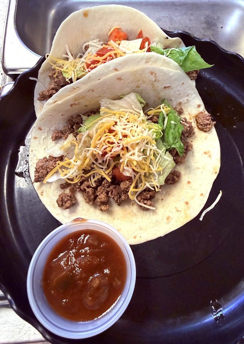 Two soft tacos with seasoned beef, lettuce, cheese and tomato, and a cup of salsa